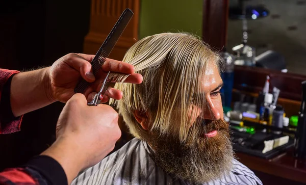 Een volwassen man in de kapperszaak. Een brutale man met een baard bij de kapper. professionele kapper met mannelijke klant. hipster met geverfd haar. De man wil een nieuw kapsel. mannelijke schoonheid en mode. Vertrouwen in zijn stijl — Stockfoto