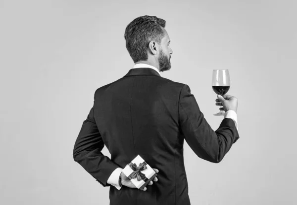 Smoking man jublar med glas rött vin hålla presentförpackning bakom ryggen för speciell dag, jubileum — Stockfoto