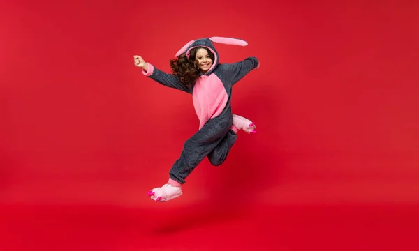 Verbaasd kind in comfortabele pyjama springen op rode achtergrond, volledige lengte, comfort — Stockfoto