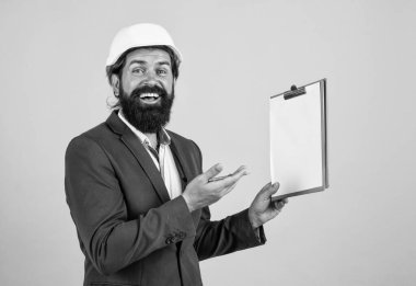 Güvenlik uzmanı. bina konsepti. Başlık takan mühendis ya da inşaatçı. Miğferli mutlu mimar notlar alıyor. Vahşi sakallı adam inşaat alanında belgelerle çalışıyor. proje üzerinde çalışmak