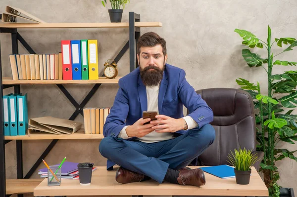 Hombre profesional con mirada perpleja mensaje de lectura en el teléfono inteligente sentado en el escritorio de la oficina, sms — Foto de Stock