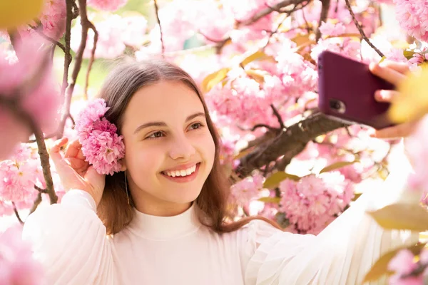 Portret szczęśliwej dziewczyny dziecko biorąc selfie na kwitnące drzewo sakura wiosną — Zdjęcie stockowe