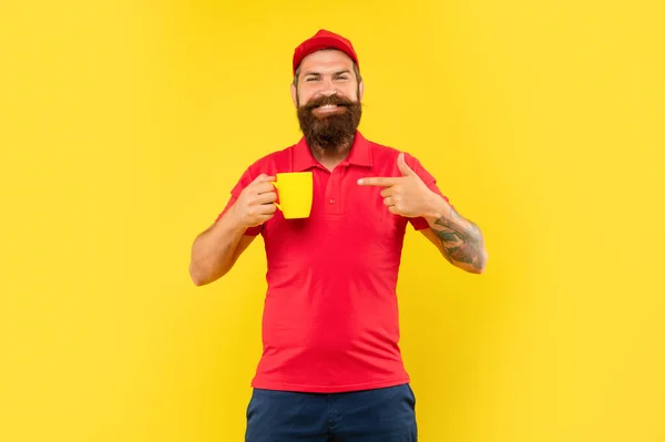 Felice uomo barbuto con berretto rosso casual e maglietta che punta il dito verso lo sfondo giallo tazza, caffè — Foto Stock