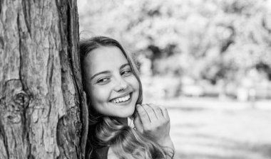 Hep gülümsüyor. Mutlu kız yaz manzarasında ağaca gülümser. Diş sağlığı. Oral bakım ürünleri. Diş bakımı. Pediatrik dişçilik. Ağız temizliğini takip et.