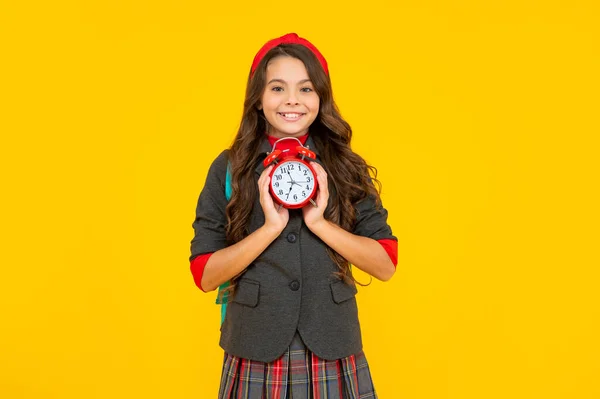 Copil în uniformă pe fundal galben. 1 septembrie: O copilărie fericită. Copil cu ceas deşteptător. — Fotografie, imagine de stoc