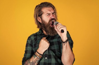Sesini yükselt. Sıradan bir adam şarkı söylerken insani duygularını ifade eder. Mikrofonlu duygusal hipster. Mikrofonlu erkek şarkıcı. Karaoke konsepti. Kareli gömlekli sakallı adam şarkı söylüyor.