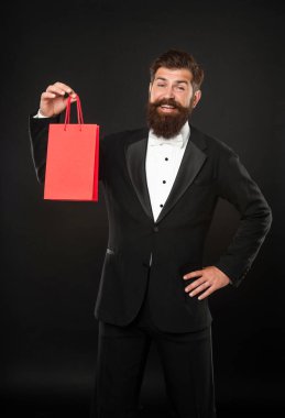 Siyah arka planda smokinli papyonlu, alışveriş çantalı gülümseyen adam. Alışveriş satışı. Boşluğu kopyala.