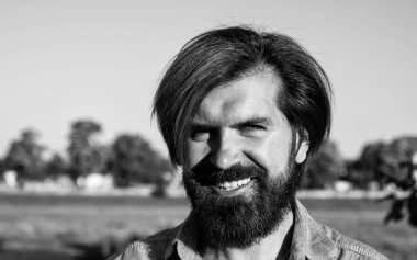 Bıyıklı vahşi sakallı erkek şık bir saç kesimi var ve açık havada günlük gömlek giyiyor, bahar.