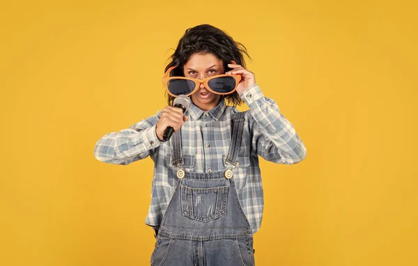 Fröhliche Dame im Hemd-Jeans-Stil singt im Mikrofon auf gelbem Hintergrund, Party — Stockfoto