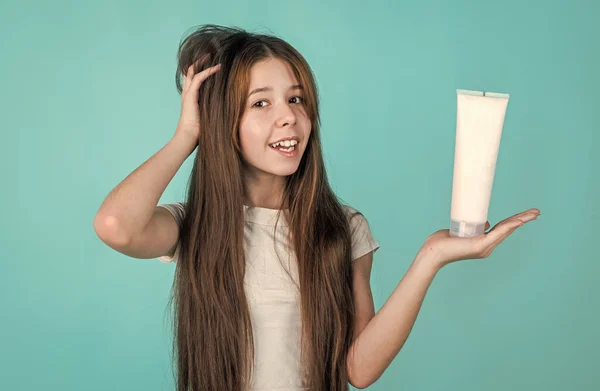 Χαρούμενο κορίτσι παιδί με μακριά ίσια μαλλιά κρατήστε conditioner σαμπουάν ή τζελ μπουκάλι, περιποίηση μαλλιών — Φωτογραφία Αρχείου