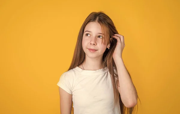 Haar schoonheid en gezondheid. schattig schoonheid heeft lang brunette haar. mode stijl. vrolijk meisje op gele achtergrond. tiener kind in casual wit shirt. kindergeluk — Stockfoto