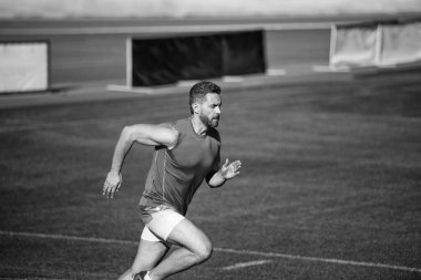 Enerjik atletik kaslı adam koşucu yeşil çimlerde koşuyor, dayanıklılık