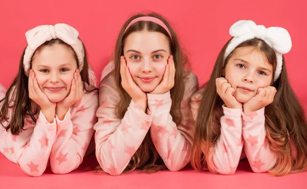 Retrato de meninas felizes deitadas com bochechas apoiadas em mãos em pijama fundo rosa — Fotografia de Stock
