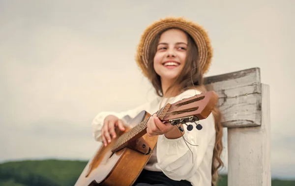 Счастливая девочка-подросток играет на акустической гитаре под открытым небом на фоне неба, музыкант — стоковое фото
