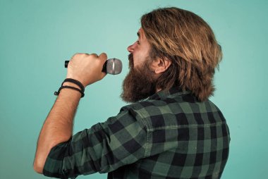 Olgun sakallı adam mikrofonla şarkı söyleyerek modaya uygun görünüyor.