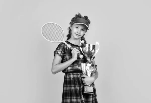 Ragazza felice che tiene attrezzature sportive. Il ragazzo tiene la racchetta da tennis. bambino indossare berretto fitness. attività infantile. stile di vita sano. Sii energico. giocatore di badminton con coppa del campionato. vincitore del campione — Foto Stock