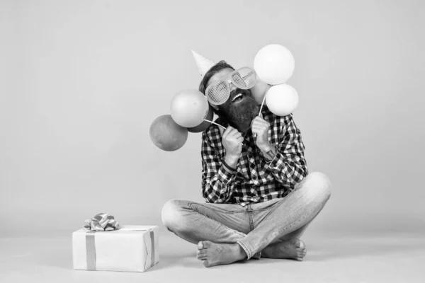 Tan bueno. hombre barbudo sentir la alegría. hombre con caja de regalo celebrando cumpleaños. hipster maduro con globos de colores brillantes. Un tipo loco y gracioso. Relajado feliz cumpleaños chico se ve alegre — Foto de Stock