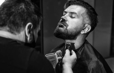 Olgun sakallı bir adamın, berber dükkanındaki kuaföre sakal tıraşı olması, yeni bir saç modeli tasarlaması.