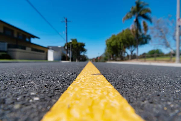 Желтая дорога с разметкой на асфальтированной дороге вдоль размытой жилой улицы в пригороде — стоковое фото