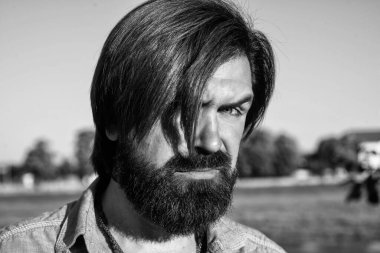 Vahşi sakallı adam günlük gömlek ve güneş gözlüğü takıyor. Erkek yaz modası ve güzellik. Bıyıklı, vahşi, beyaz bir hippi. Kendine güvenen ve yakışıklı adam bahar portresi