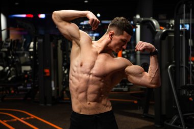 Formda, kaslı, kaslı, kaslı, spor salonunda çift kol pozu veren güçlü bir adam.