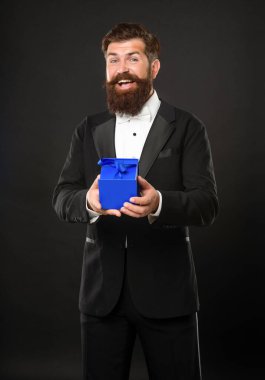 Smokinli, papyonlu, siyah arka planda, hediye kutulu neşeli bir adam. Boks günü