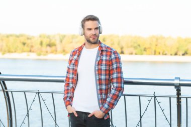 Dişli gömlekli ve kulaklıklı genç sakallı adam.