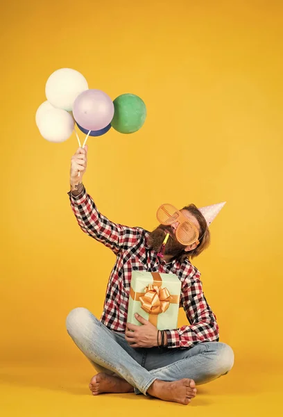 Branco hipster maduro com óculos de festa engraçados em camisa quadriculada segurando balões e caixa de presente, celebração — Fotografia de Stock