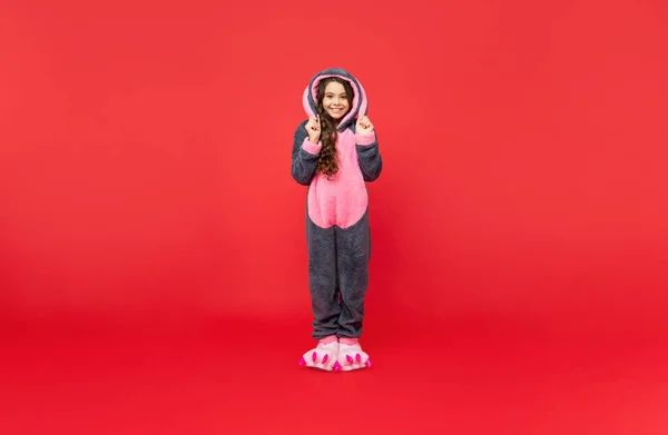 Cheerful kid in comfortable pajama on red background, full length, home — Stock Photo, Image