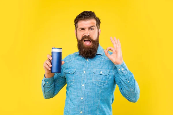 Ammiccante brutale uomo barbuto tenere bottiglia di shampoo su sfondo giallo, presentando articoli da toeletta. Ok. — Foto Stock