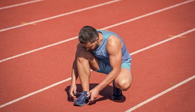 Stadyumda egzersiz yaptıktan sonra ayakkabı bağcıkları bağlayan bir adam. Spor salonu açık havada. Kaslı atletizm antrenmanı. Spor. Erkek fitness modası. Sporcunun molası var. Sporcuların rahatlamaya ihtiyacı var