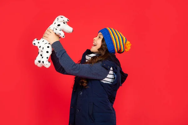 Criança feliz na jaqueta de puffer segura o brinquedo. menina adolescente no fundo vermelho. infância feliz. criança brincando brinquedo — Fotografia de Stock