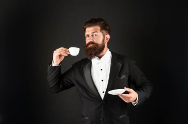 Smokin giymiş, papyonlu, kahve fincanı takan ciddi bir garson. Resmi giyinen beyefendi kahve içer.