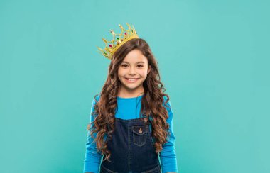 Kıvırcık saçlı, mavi arka planda kraliçe tacıyla mutlu çocuk, bencillik.