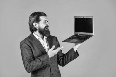 Ürün sunumu. Bilgisayarlı mutlu beyaz sakallı hippi. Erkek çalışanın elinde finans raporu ve laptopta ortak çalışma alanı araştırmaları var. Modern iş dünyasındaki yeni teknoloji yalan söylüyor