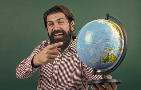 あそこを見て。学校に戻って。非公式教育。幸せな成熟した先生が地球を指しています。髭の男地理学者は地図付きの教室で働いてる。試験の準備を。地理の授業で大学の講師が — ストック写真