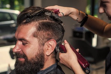 Zevkle tıraş oluyorum. Hipster. Erkek berber bakımı. Kuaför salonundaki sakallı adam. Güzellik ve moda. Saç ve sakal şekillendirme. Profesyonel berber ustası olan vahşi adam elektrikli tıraş makinesi kullanıyor.