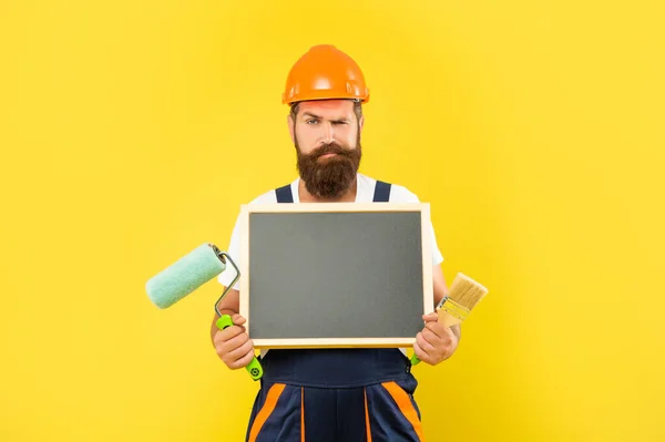 Mann Hausmaler in Helm und Arbeitskleidung hält Farbroller und Tafel mit Kopierraum — Stockfoto