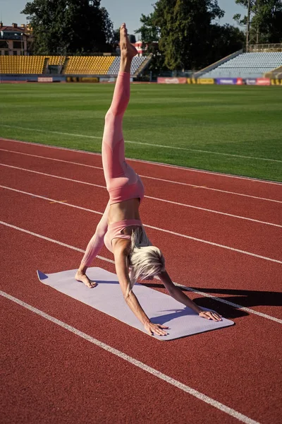 Elastyczna kobieta rozciągająca się na stadionie w odzieży sportowej, jodze — Zdjęcie stockowe