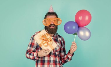 Havalı saç stili olan şık sakallı adam kareli gömlek giyiyor parti balonları ve hediye kutusu, mutluluk.