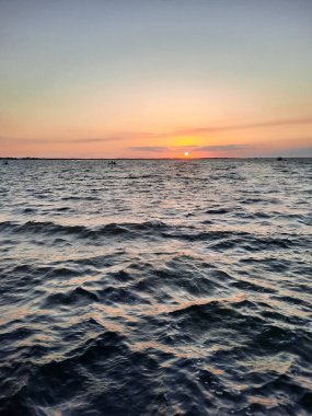 Gün batımında akşam gökyüzü altında deniz dalgaları olan bir su manzarası