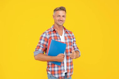 Okul kitaplarını sarı arka planda tutan gündelik parmakla işaret eden mutlu çocuk, öğrenci.