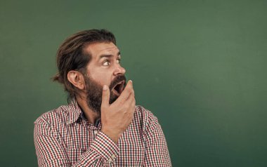 Kafkas hippiler yeşil arka planda şaşkınlık hissederler. kopyalama alanı. Tahtanın arka planında olgun bir öğretmene sürpriz oldu. Vahşi sakallı adam sıradan bir kareli gömlek giyer. insan duygularını ifade etmek