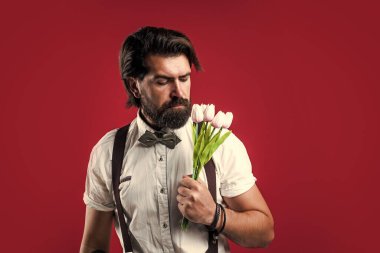 Bahar çiçeği hediyesi. Askılı ve papyonlu romantik bir adam. Kendine güvenen ve zarif bir adam lale çiçekleri tutar. Aşk randevusu için hediye. Buketli eski moda sakallı hippi.