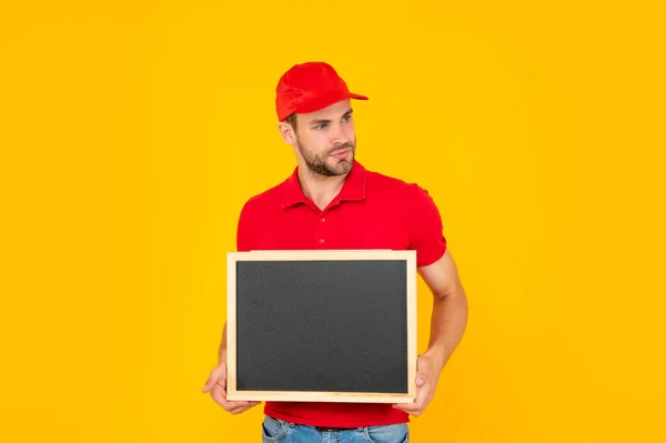 Unshaven giovane uomo in camicia rossa tenere lavagna con spazio copia su sfondo giallo, annuncio — Foto Stock