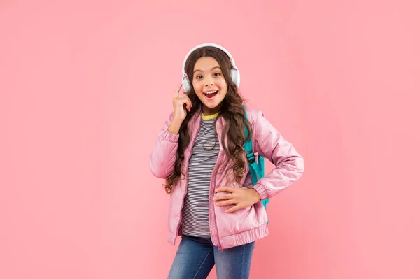 Дивує дитину слухати музику в навушниках і носити рюкзак на рожевому фоні, освіта — стокове фото