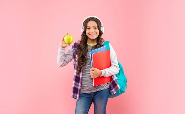 De vuelta a la escuela. feliz adolescente chica en auriculares celebración de manzana. escuchar música. nueva tecnología. —  Fotos de Stock