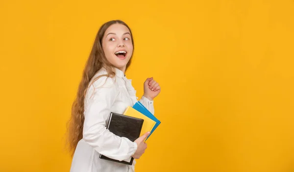 Překvapený šťastný běh dítě se školní domácí úkol na žlutém pozadí s kopírovacím prostorem, dětství — Stock fotografie