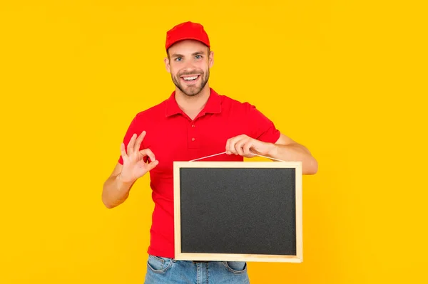 Neoholený mladý muž v červené košili držet tabuli s kopírovacím prostorem na žlutém pozadí, reklama — Stock fotografie