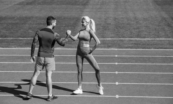 Hombres y mujeres deportistas socios de fitness celebran la victoria del equipo con el gesto de estrechar la mano después de hacer ejercicio o competir en la lucha libre en el estadio pista de atletismo arena al aire libre, el éxito deportivo. — Foto de Stock